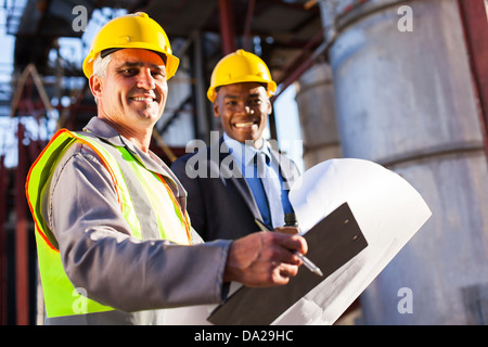 Senior industria petrolifera lavoratore negli appunti di contenimento e blueprint con manager in una pianta Foto Stock