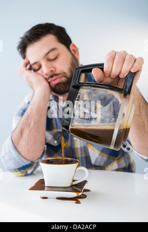 Stanco, sleepy uomo la fuoriuscita di caffè sul tavolo Foto Stock