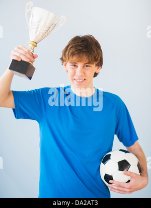 Ragazzo adolescente (14-15) trattenere la sfera e il trofeo Foto Stock