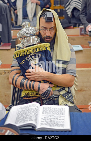 Un uomo che indossa una preghiera scialle & phylacteries tenendo un Torah durante la mattina dei giorni feriali servizi in sede Lubavitch in NYC Foto Stock