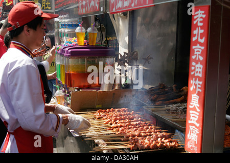 L'uomo cuocere carne su bastoni, Wangfujing street, Pechino, Cina Foto Stock