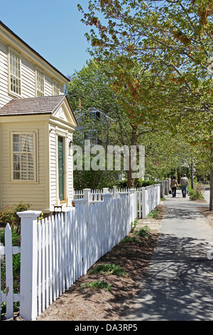 Una casa gialla dietro un white Picket Fence, nella concordia, Massachusetts, due persone camminando sul marciapiede in distanza. Foto Stock