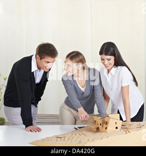 Tre studenti di architettura discutendo 3D modello di edificio sulla scrivania Foto Stock