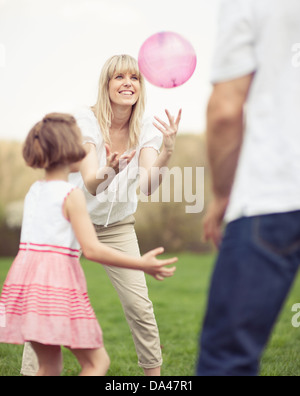 Padre madre e figlia lanciando la palla a vicenda nel parco Foto Stock