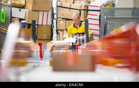 Un membro del personale della Deutsche Post DHL il servizio di spedizione pacchi posti su un nastro trasportatore alla recente apertura di spedizioni hub di DHL a Berlino, Germania, 3 luglio 2013. La struttura ha la capacità di elaborare fino a 8000 pacchetti e pacchi al giorno. Foto: Hannibal Hanschke Foto Stock