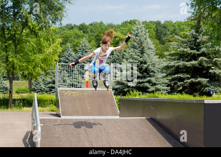 Agile giovane femmina skater rullo jumping metà aria come Lei viaggia verso il basso una rampa di cemento in una zona rurale skate park Foto Stock