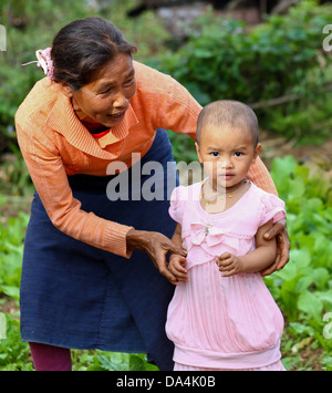 Giovani burrmese triste, come la madre è lontano a lavorare in Thailandia, ragazza con sua nonna di fronte orto familiare Foto Stock