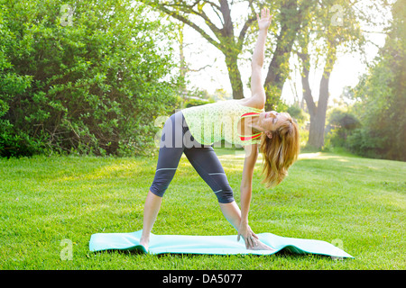 Femmina istruttore di fitness facendo yoga triangolo esteso pongono all'aperto nel parco verde Foto Stock