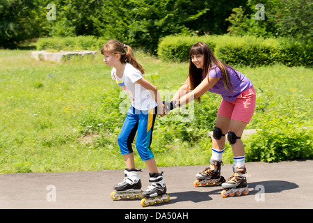 Due attraenti adolescente amici femmina pattinaggio con uno tira l'altra lungo dietro di lei in un lussureggiante parco rurale Foto Stock