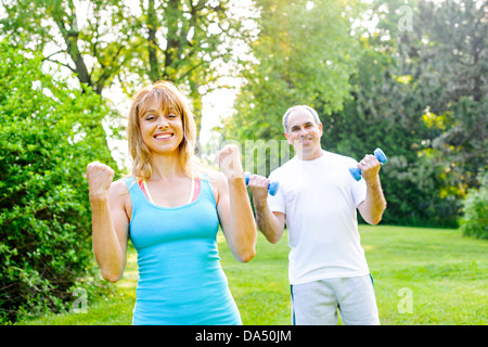 Femmina istruttore di fitness esercizio con uomo di mezza età in parco verde Foto Stock