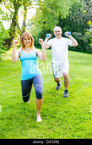 Femmina istruttore di fitness esercizio con uomo di mezza età in parco verde Foto Stock