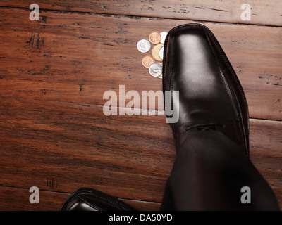 Primo piano della calzatura uomo in piedi sulle monete, denaro trovato sul concetto di pavimento Foto Stock