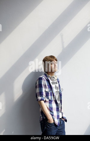 Giovane uomo appoggiata contro il muro bianco ascoltando musica sulle cuffie Foto Stock