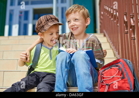 Due fratelli felice con libro e zaino sulle scale di fronte scholl. Foto Stock