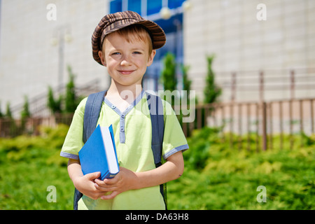 Carino giovane Ragazzo con libro di fronte all edificio scolastico. Foto Stock