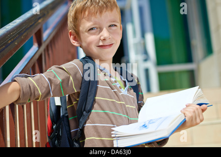 Giovane Ragazzo con libro di fronte all edificio scolastico Foto Stock