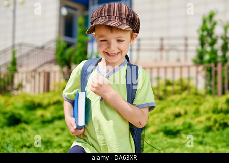 Carino giovane Ragazzo con libro di fronte all edificio scolastico. Foto Stock