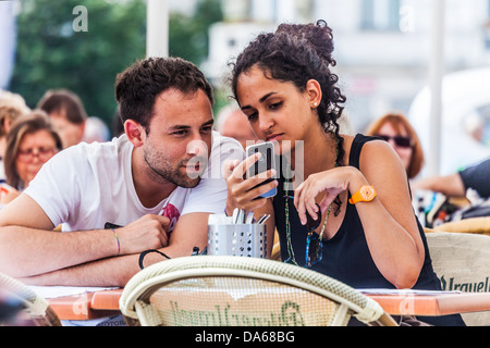 Un attraente coppia giovane utilizzare il loro iPhone mentre è seduto in un cafe' all'aperto in Piazza della Città Vecchia di Praga Foto Stock