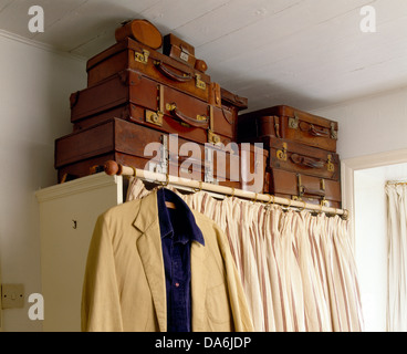 Pelle Vintage valigie impilato al di sopra della semplice con la camicia appesa in pole con crema di tende Foto Stock