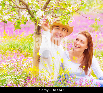 Famiglia giovane avendo divertimento all'aperto, carina ragazza con ragazzo attraente cercando su fiori che sbocciano, rapporto romantico, il concetto di amore Foto Stock