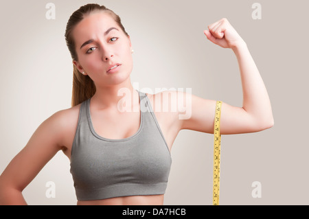 Potente donna misurando il suo bicipite con un giallo nastro di misurazione Foto Stock