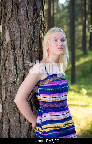 Zoomed donna in abito foderato poggia su albero Foto Stock