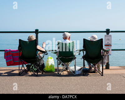 Tre persone anziane in campeggio sedie seduti sul lungomare a Sidmouth, nel Devon, Inghilterra Foto Stock