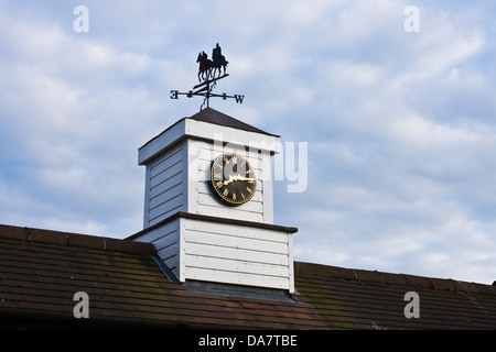 Una banderuola con un motivo delle corse ippiche si siede sulla cima di una torre dell'orologio sul tetto di un edificio in un prigioniero. Foto Stock