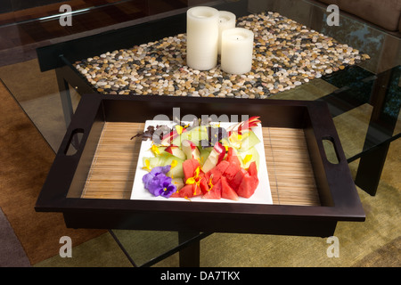 Un piatto di frutta seduta sul tappetino di bambù con le candele sulla tabella di caffè di vetro Foto Stock