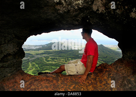 Un escursionista prende in vista della valle di Nuuanu dai pali Puka, un foro nel lato della montagna Giugno 29, 2013 in Oahu, Hawaii. Foto Stock