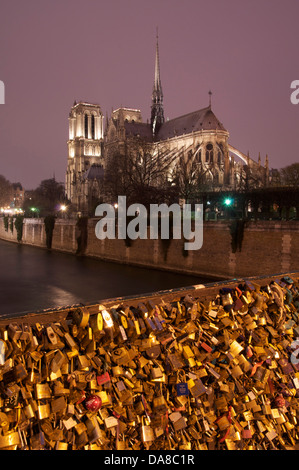 La gotica Cattedrale di Notre Dame illuminata al tramonto, visto attraverso la Senna dal Pont de Sully. Lucchetti dell amore festone la ringhiera. Parigi, Francia. Foto Stock