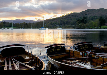 Una scena del tramonto su Windermere con bei raggi di sole si diffonde in tutto il cielo e con le barche a remi in primo piano. Foto Stock