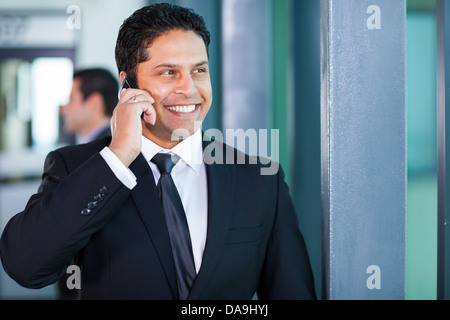 Bel giovane imprenditore indiano parlando al telefono cellulare in ufficio Foto Stock