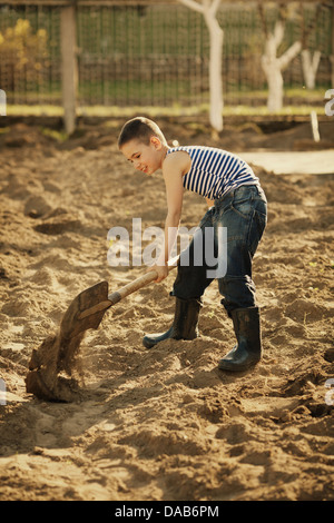 Poco felice ragazzo lavora con pala in giardino Foto Stock