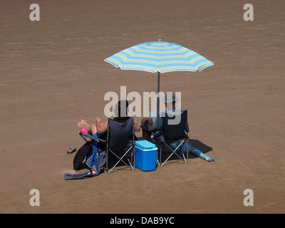 Giovane si sedette sotto una grande tenda da sole ombrellone in spiaggia, Burnham on sea, Somerset, Regno Unito 2013 Foto Stock