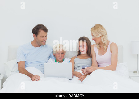 Famiglia seduta sul letto e utilizzando un computer portatile Foto Stock