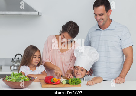 I bambini guardando la loro madre che è il taglio di vegetali Foto Stock