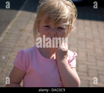 Carino ragazza carina bambina in piedi sul percorso con un top rosa e lei è scrathing il suo volto con la sua mano sinistra. Foto Stock