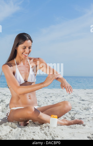 Donna sorridente seduto sulla spiaggia l'applicazione di crema solare Foto Stock