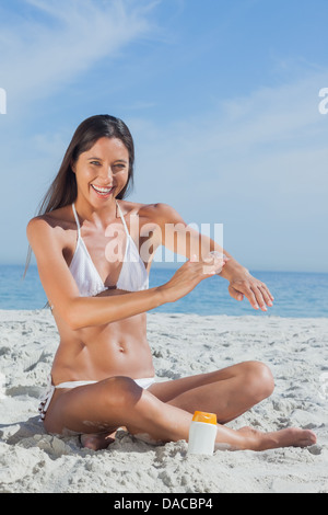 Felice donna seduta sulla spiaggia l'applicazione di crema solare Foto Stock