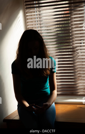 Una silhouette di una ragazza adolescente, seduti in una finestra. Foto Stock