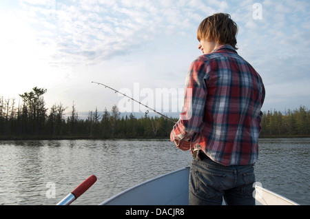 Teen maschio di pesca al largo della parte posteriore di una riga barca su un piccolo entroterra del lago. Foto Stock
