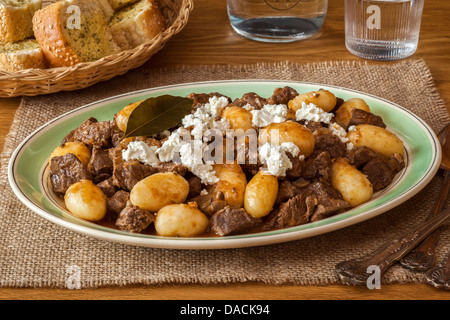 Greco stufato di agnello o Stifado, conditi con formaggio feta sbriciolato, servita con pane all'aglio. Foto Stock