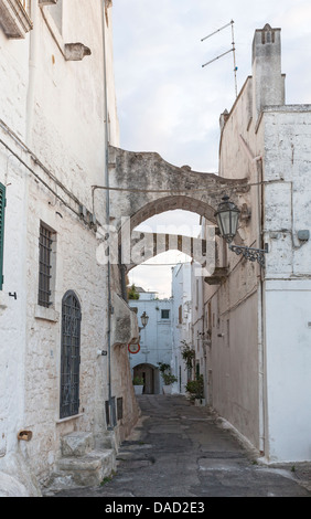 Vicolo di Ostuni storico centro medievale città vecchia, Puglia, Italia meridionale, con due arcate e un vecchio lampione Foto Stock