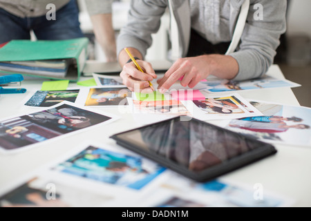 Giovane uomo rendendo note sulla scrivania di fotografie con tavoletta digitale in ufficio creativo Foto Stock