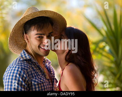 Giovane donna baciare uomo che indossa cappello per il sole, sorridente Foto Stock
