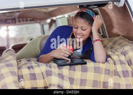 Giovane donna con tavoletta digitale in camper van, sorridente Foto Stock