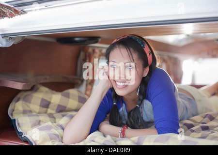 Giovane donna sdraiata nel retro del camper, sorridente Foto Stock