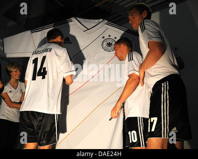 Nazionale tedesco di calciatori di Holger Badstuber (L-R), Lukas Podolski e Per Mertesacker firmare un sovradimensionato jersey durante la presentazione del nuovo Euro 2012 maglie presso una concessionaria auto ad Amburgo, Germania, 09 novembre 2011. La selezione tedesca giocherà in Ucraina in un test match a Kiev il 11 novembre 2011 e i Paesi Bassi ad Amburgo il 15 novembre 2011. Foto: Cristiano C Foto Stock