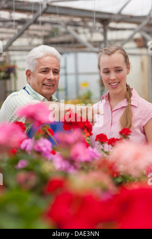 Senior giardiniere che serve metà donna adulta nel centro giardino, sorridente Foto Stock